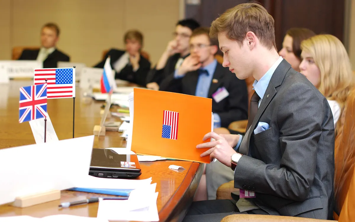 A delegate in a suit reading his papers at a Model United Nations committee table, with small flags and a United States placard in front of him