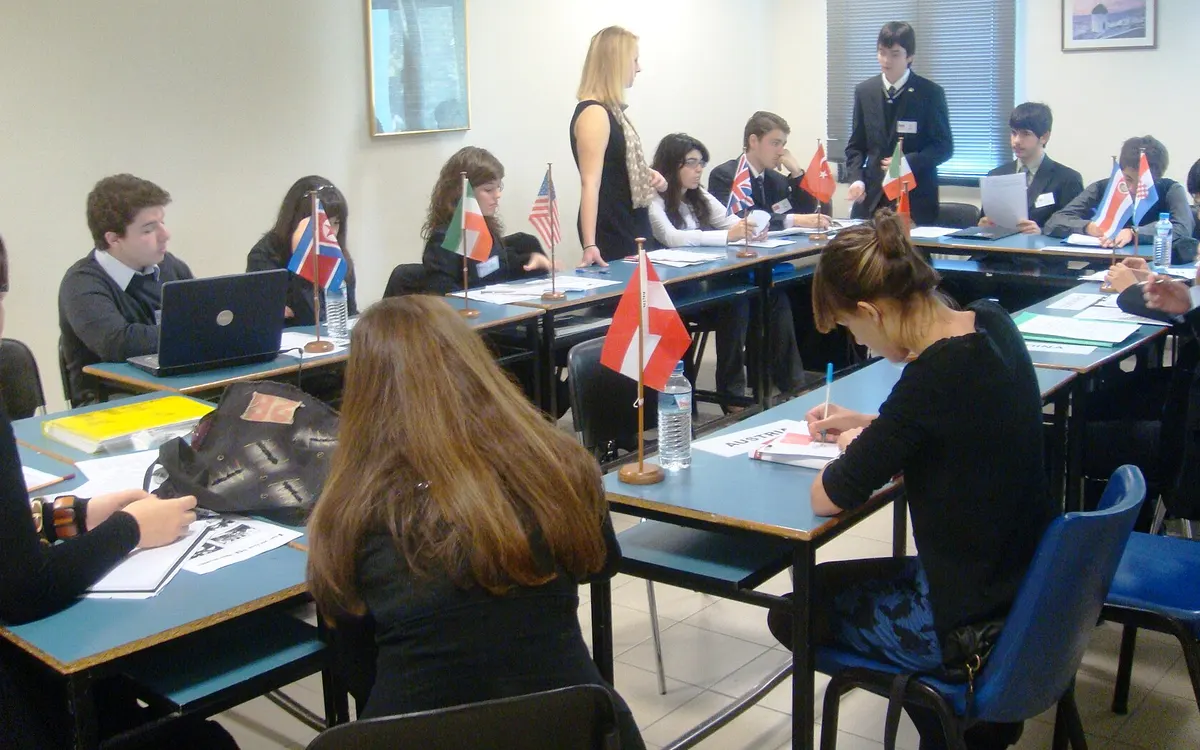 Students at Thessaloniki Model United Nations working at their laptops around a council table with small national flags