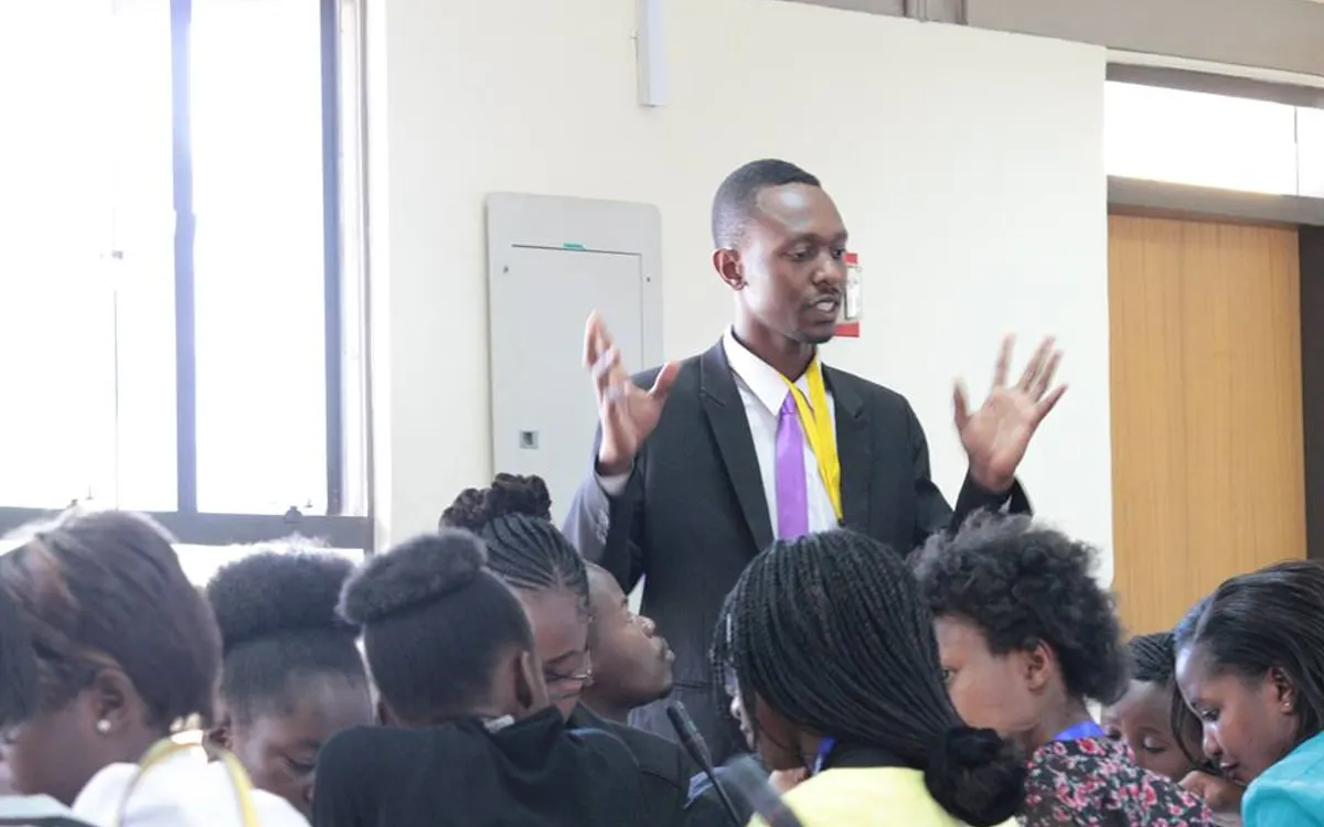 A delegate standing and speaking with his hands raised to a group of seated delegates during an unmoderated caucus