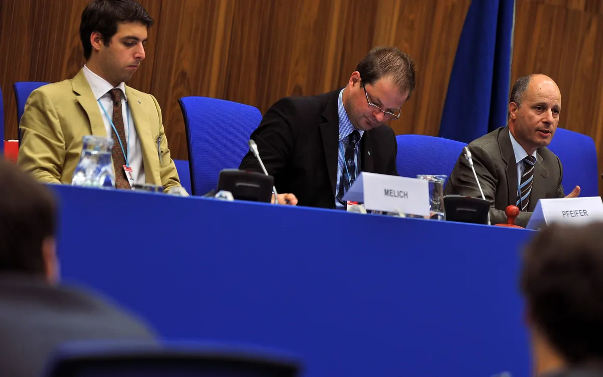 The dais of a committee at the Vienna International Model United Nations: three men in suits seated behind a long table with microphones