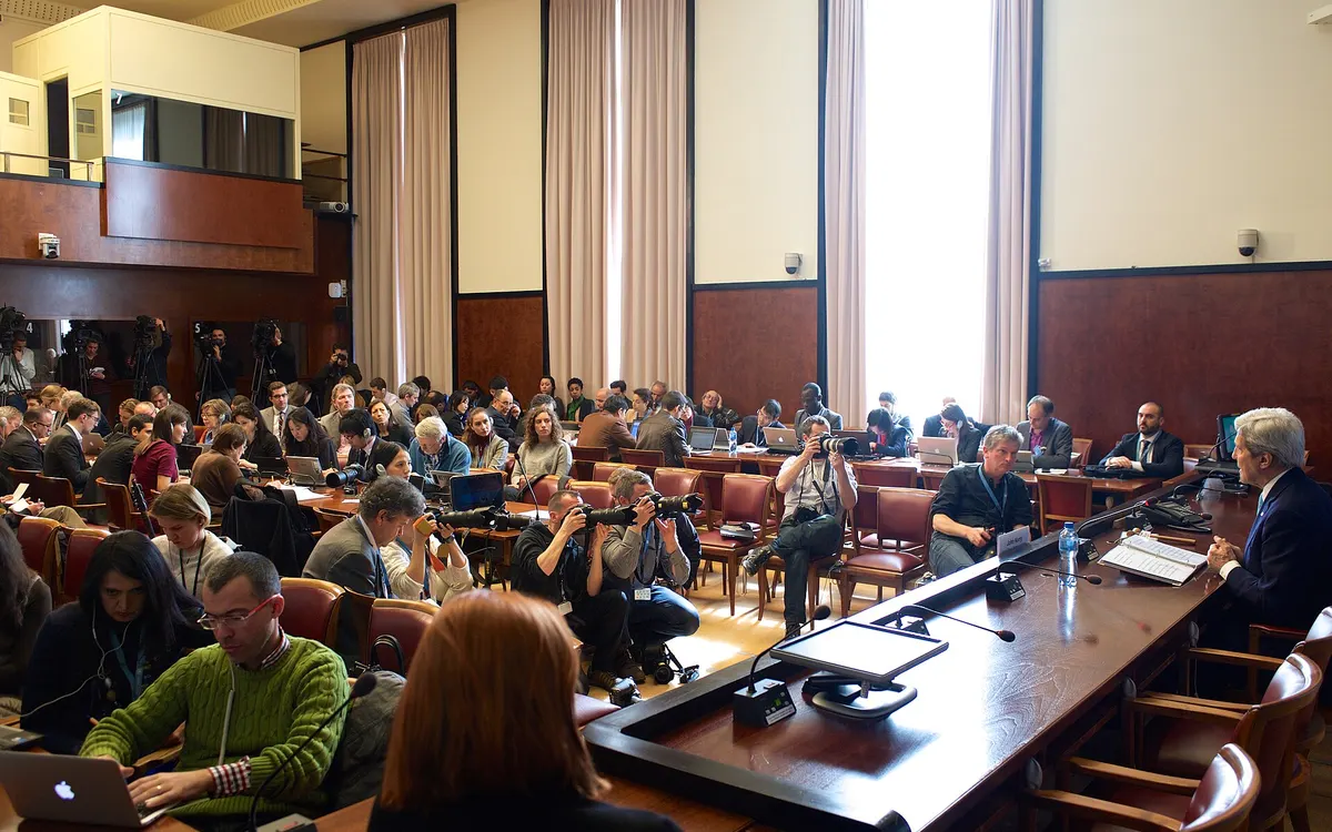 Journalists seated at a press conference in a meeting room at the United Nations in Geneva, with a speaker at a table at the front